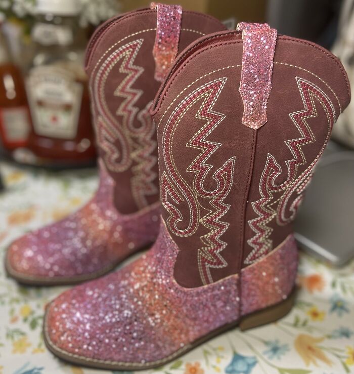 Pink glitter cowboy boots with decorative stitching, shown on a floral surface as a weird Amazon pick.