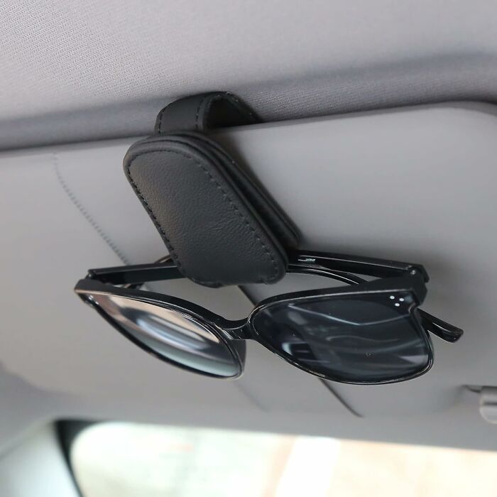 Black sunglasses clipped to a leather car accessory attached to the vehicle's sun visor for convenient storage.