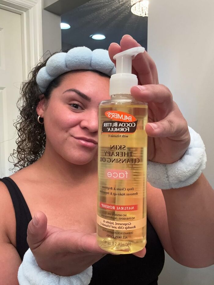 Person holding a bottle of skin therapy cleansing oil, featuring low-effort products for high-anxiety body issues.