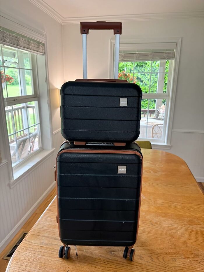 Black hard-shell luggage set with brown accents and telescoping handle, showcased indoors on a wooden table, Prime Day treasures.