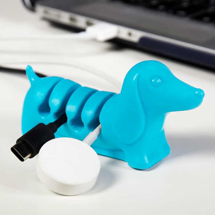 Blue dachshund-shaped cable organizer holding USB and charging cords on a desk near a keyboard, showing usefulness.
