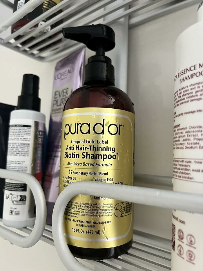 Pura d'or anti hair-thinning biotin shampoo bottle on a shower shelf, a top-rated Prime Day find.