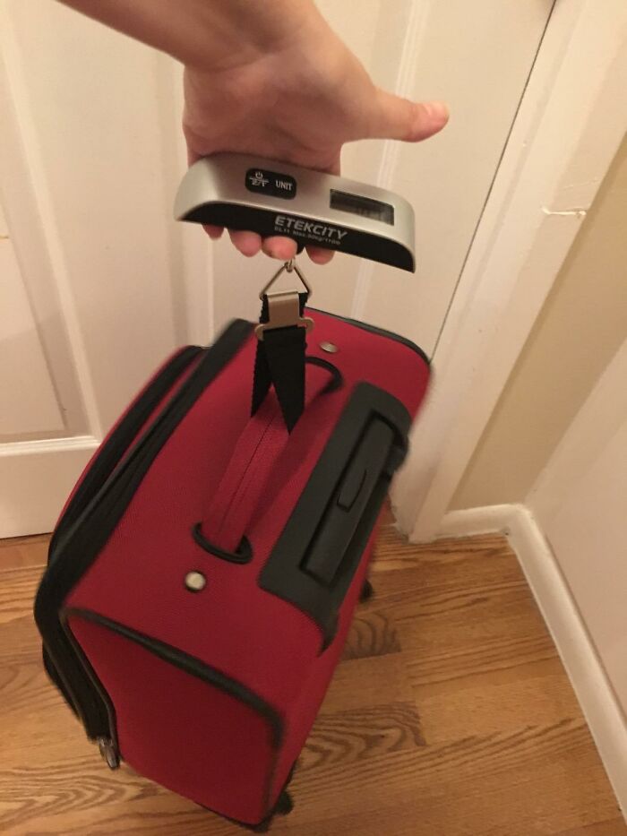 Hand weighing red suitcase with digital luggage scale, showcasing expert-approved travel finds to ditch travel drama.