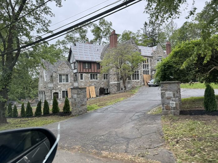Stone house under renovation with boarded-up windows and visible roof work, a failed creative home project example.