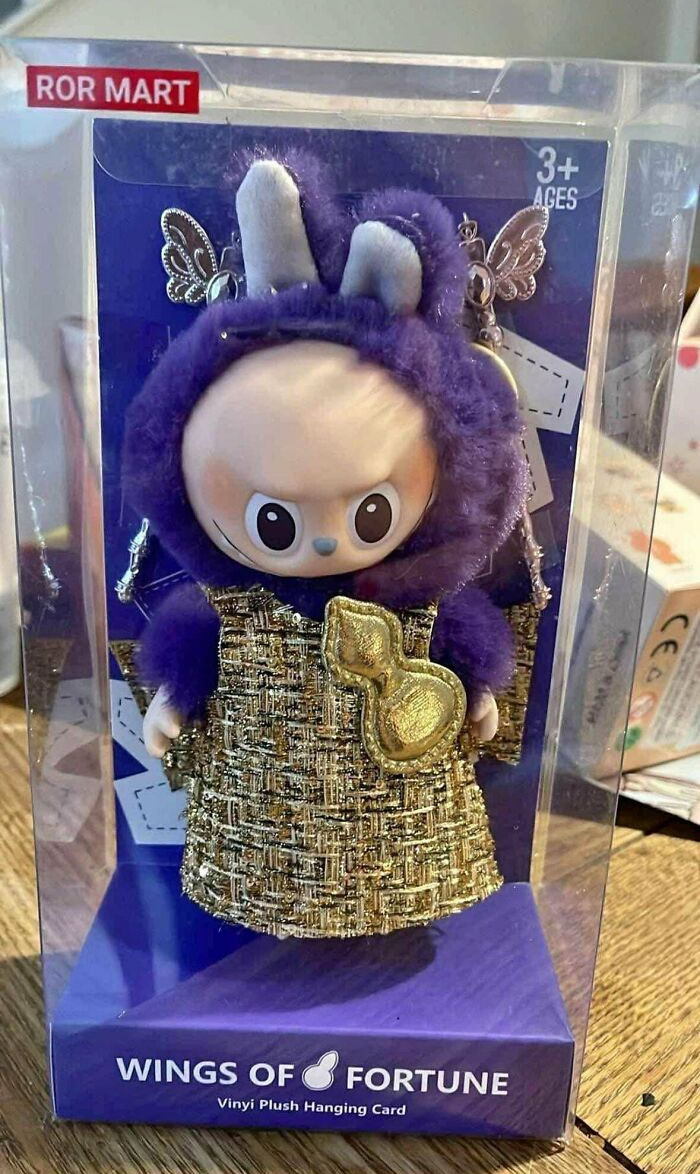 Creepy Labubus fake plush doll with large eyes and purple outfit in clear packaging, Wings of Fortune toy design.