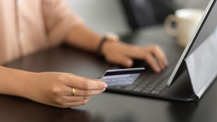 Person holding a credit card and using a tablet, symbolizing a bride trying to cancel a guest’s resort room. - 1