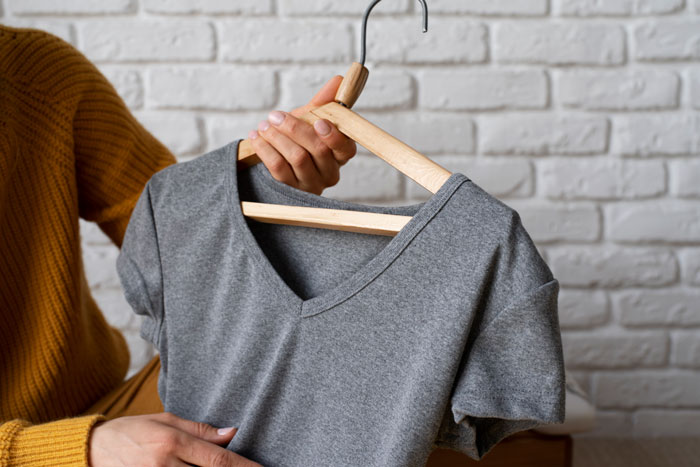 Person holding a grey shirt on a hanger, illustrating unexpected things people learned about the rich lifestyle.