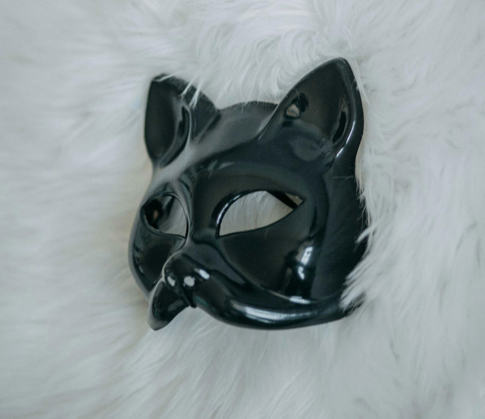 Black cat mask resting on white fur, symbolizing a mysterious figure in a full-body cat suit at night.