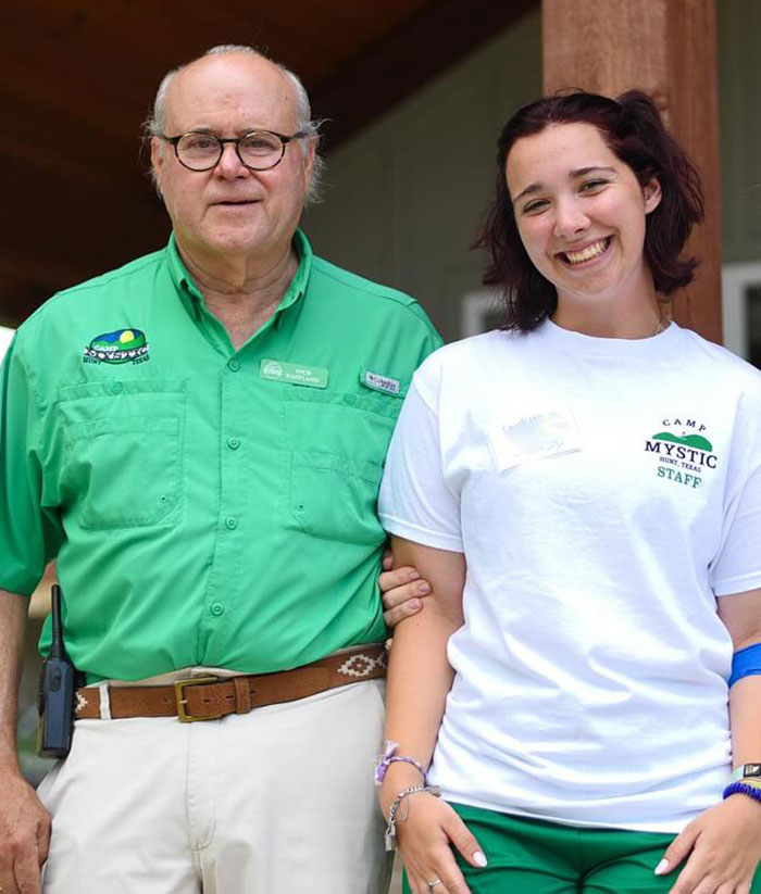 Camp Mystic counselor smiling beside a man in a green shirt, sharing a heartfelt moment at the camp location.