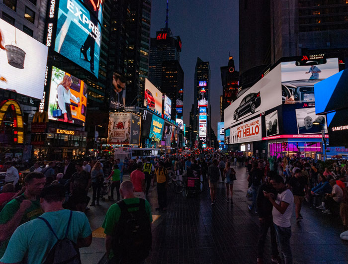 Crowded public space at night with brightly lit billboards, illustrating women sharing inappropriate comments from men.