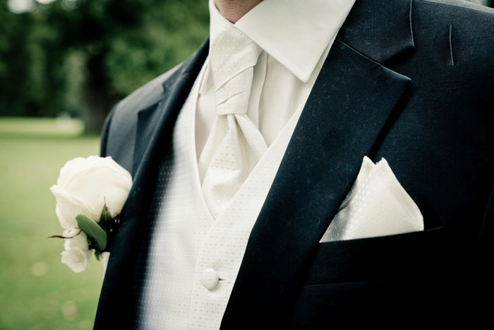 Close-up of a groom wearing a black suit with white tie and boutonniere, related to wedding invitation regrets. - 27