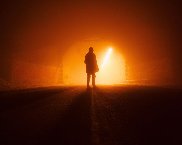 Silhouetted figure in a foggy tunnel with eerie orange light, evoking real-life horror stories and unexplainable encounters. - 9