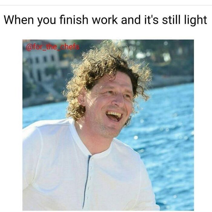 Happy chef laughing outdoors by water, relatable chef meme about finishing work while it’s still light outside.