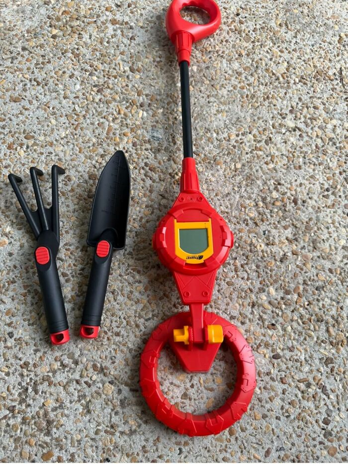 Black and red gardening tools and a red digital metal detector on a textured stone surface, showcasing weirdest picks on Amazon.