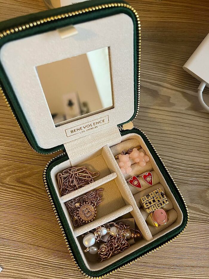 Compact travel jewelry case open on wooden surface, showcasing earrings and necklaces as travel essentials.