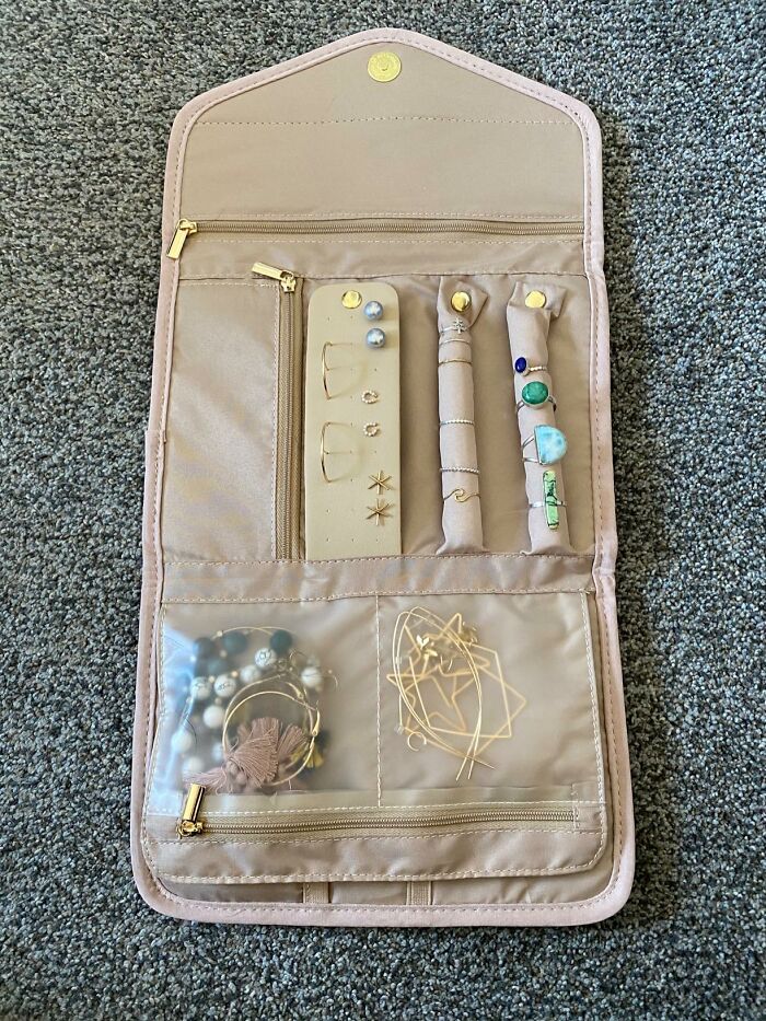 Beige travel jewelry organizer with earrings, rings, and bracelets neatly stored on a carpet surface for travel drama relief.