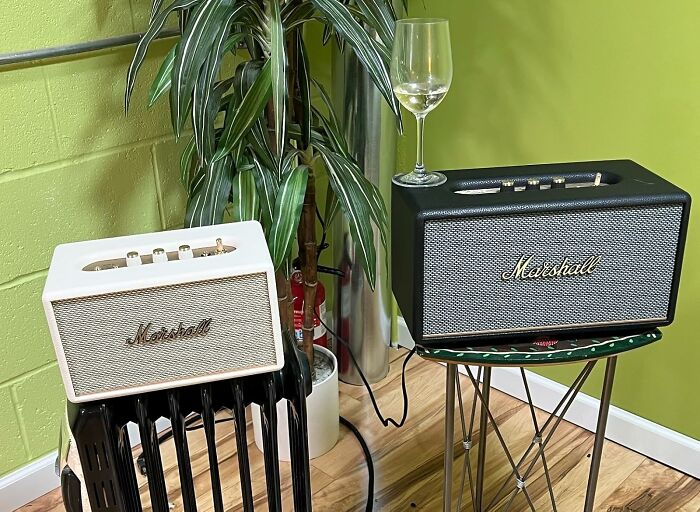Two retro Marshall speakers placed on black heater and small green table, with a glass of wine on top, in a cozy room.