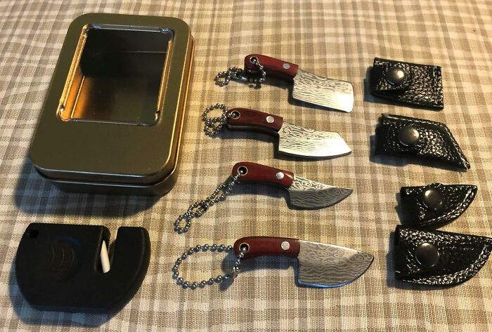 Miniature utility knives with sheaths and a small metal storage tin displayed on a checkered surface.