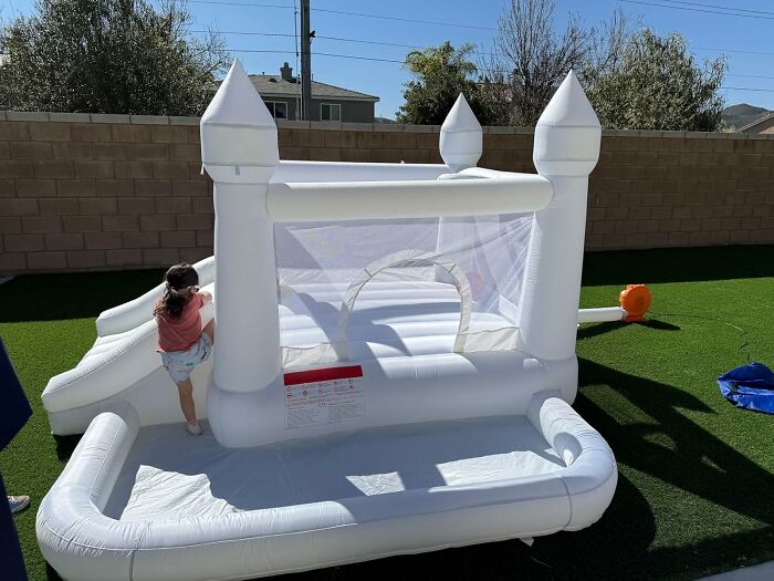 Child climbing on a white inflatable bounce house with slide in backyard, a weird Amazon pick with unique features
