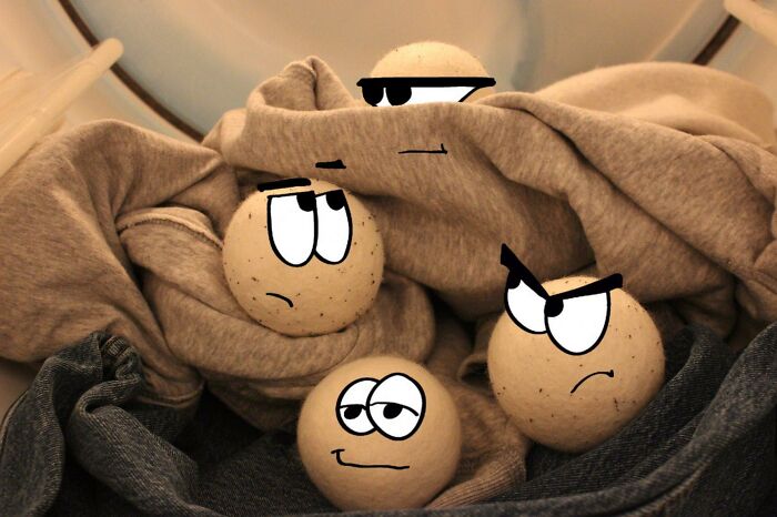 Four laundry dryer balls with cartoon faces showing suspicion and spying expressions among clothes inside a dryer.