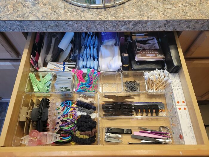 Organized drawer with clear compartments holding toiletries, hair accessories, and grooming tools for home organization products.