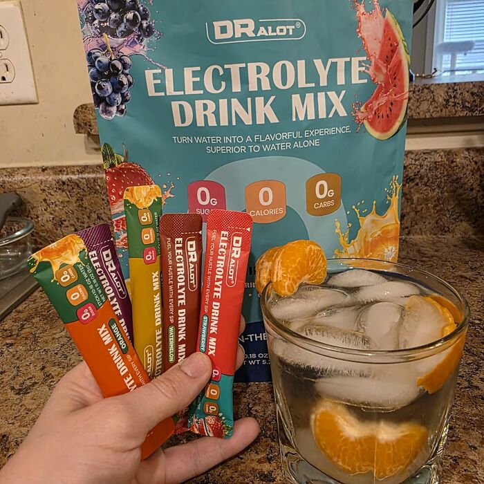 Electrolyte drink mix packets and iced water with orange slices on a kitchen counter for heatwave survival hacks.