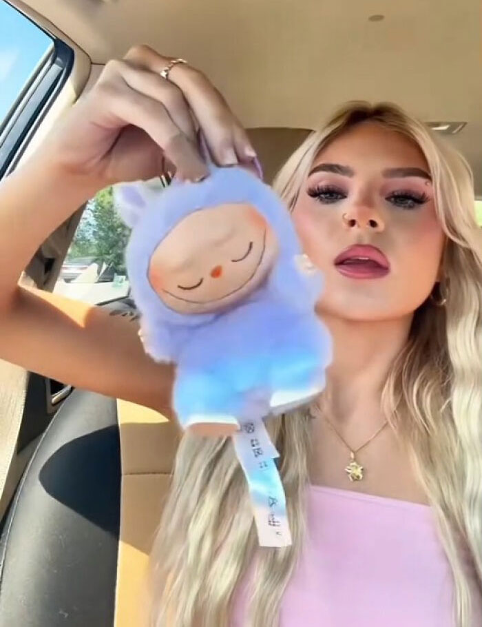 Young woman holding a creepy Labubus fake doll inside a car, highlighting unsettling toy replicas that might cause nightmares.