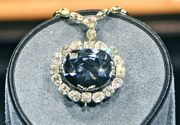 Oval blue diamond necklace surrounded by diamonds displayed on a gray velvet stand, highest-value collectible item sold.