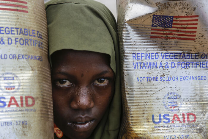 Close-up of a person between large, worn vegetable oil containers showing consequences of their own stupidity at work.