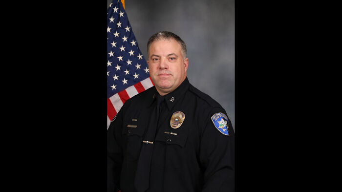 Police officer in uniform posing for official portrait with American flag, illustrating consequences of job-related mistakes.
