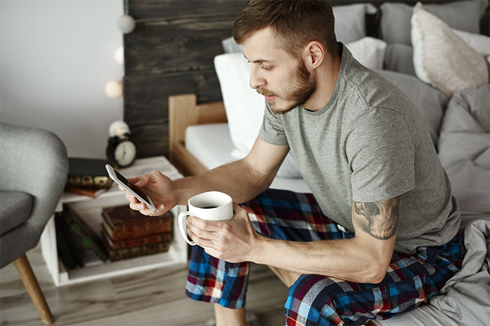 Man in pajamas holding coffee and looking at phone, reflecting on AI girlfriend impacting his marriage and relationship. Man in pajamas holding coffee and looking at phone, reflecting on AI girlfriend impacting his marriage and relationship.