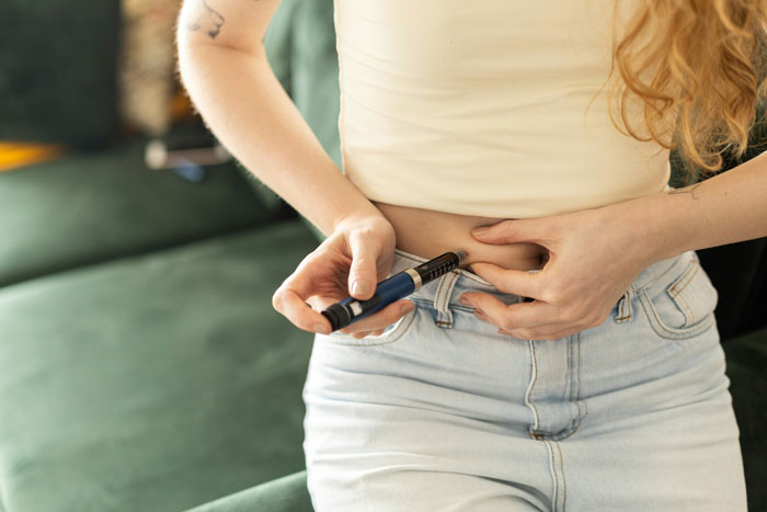 Woman holding weight loss medication pen near abdomen, illustrating doctor prescribed treatment for weight loss. Woman holding weight loss medication pen near abdomen, illustrating doctor prescribed treatment for weight loss.