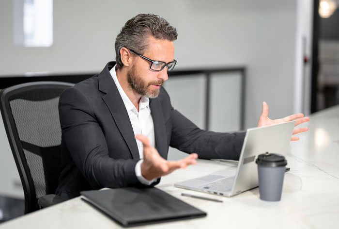 Man in a suit looking frustrated at laptop, illustrating boss told guy to message after every client situation. - 17