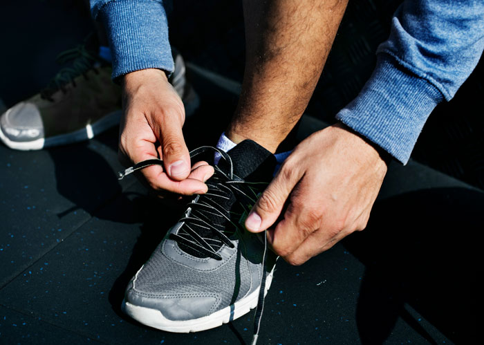 Person tying shoelaces on athletic shoe, illustrating practical tips to stay safe and alive in everyday activities.
