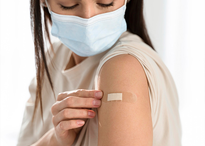 Person wearing a mask applying a bandage on arm after vaccination, symbolizing facts people are tired of explaining