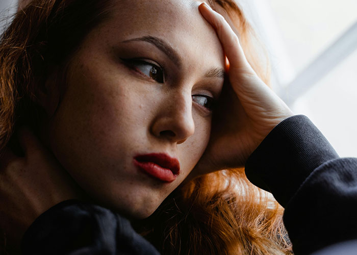 Close-up of a woman with red hair looking thoughtfully out a window, conveying emotions linked to cheating stories.