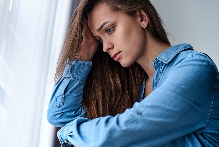 Woman looking thoughtful and pensive near a window, illustrating emotions of women who married rich sharing their experiences.