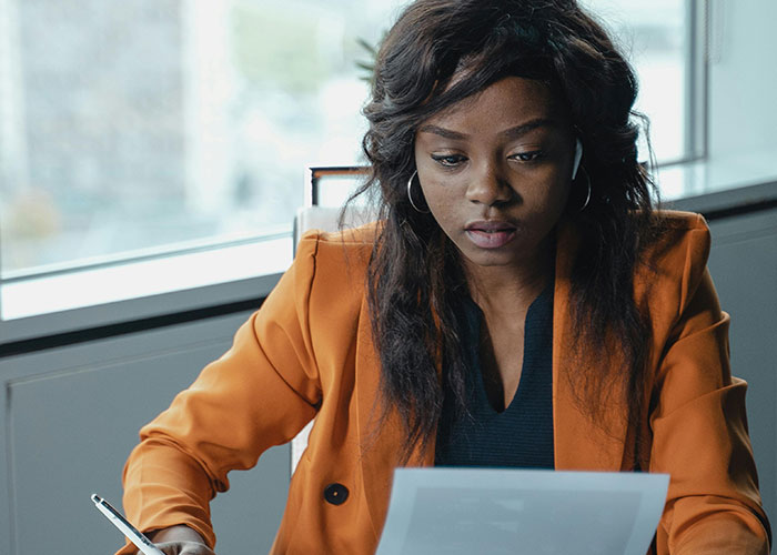 Young professional woman in an orange blazer reviewing documents, highlighting signs of micromanagement in the workplace.