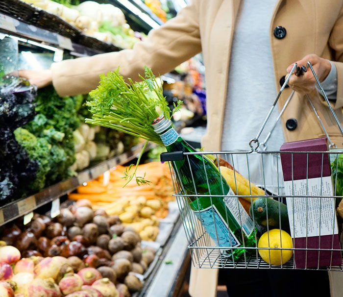 Woman shopping in grocery store holding basket with fresh produce, highlighting women and inappropriate comments in public spaces.