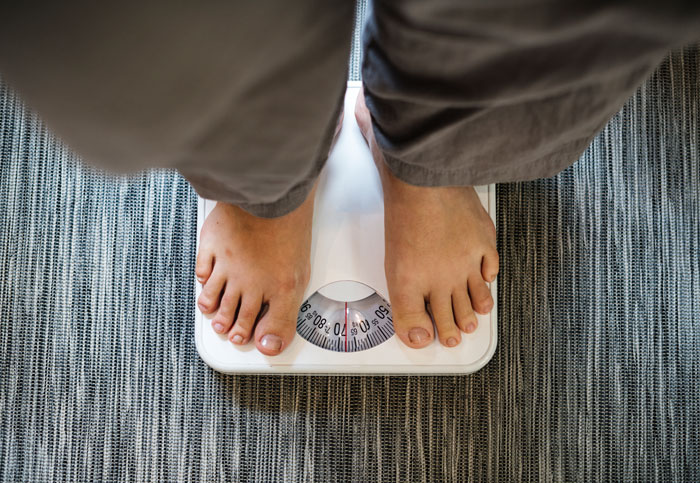 Person standing on a white scale measuring weight, illustrating obesity and health concerns in Americans. - 8