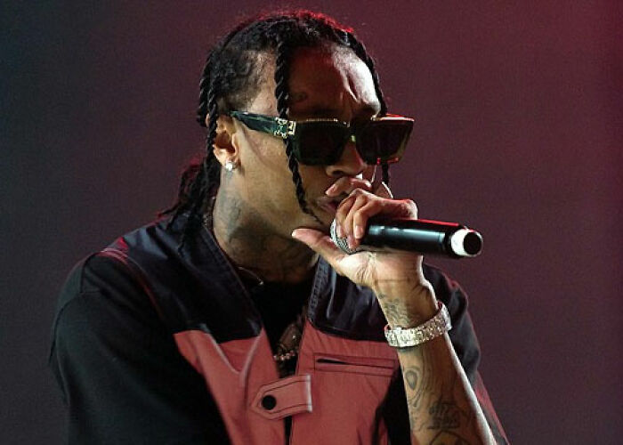 Rapper performing on stage, wearing sunglasses and a pink and black jacket, related to KarJenner clan controversies. - 16