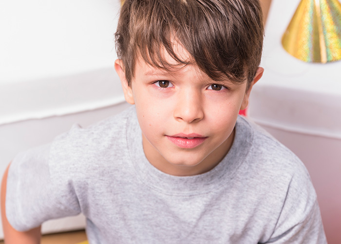Young boy looking at camera with a slight smile, illustrating parents revealing hilarious lies they tell their kids.