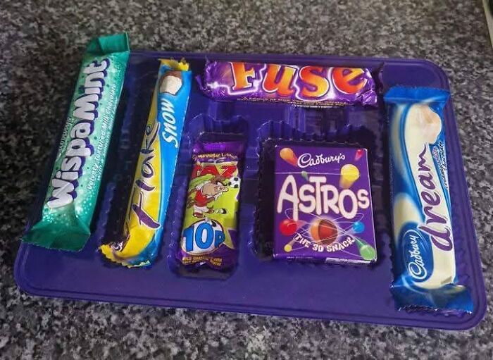 Selection of nostalgic 90s UK chocolate bars on a purple tray, capturing the magic of growing up in the ’90s.