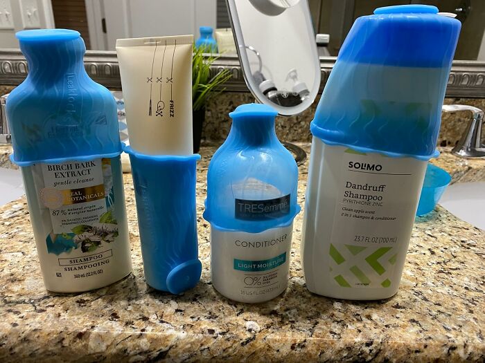 Shampoo and conditioner bottles with blue silicone travel covers lined up on a bathroom countertop for travel essentials.