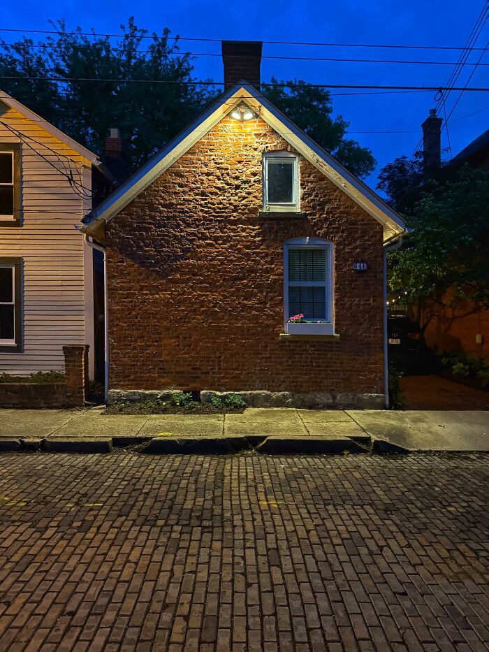 Small brick house with oddly placed windows on a quiet street, showing a failed creative home design attempt at night.
