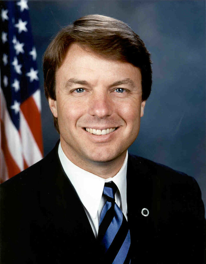 Portrait of a smiling man in a suit and tie with an American flag in the background, symbolizing true interesting rumors.