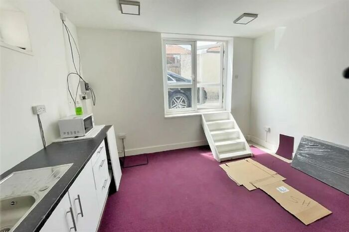 Small room with purple carpet, white kitchen cabinets, and a makeshift staircase, showcasing creative home design fail.