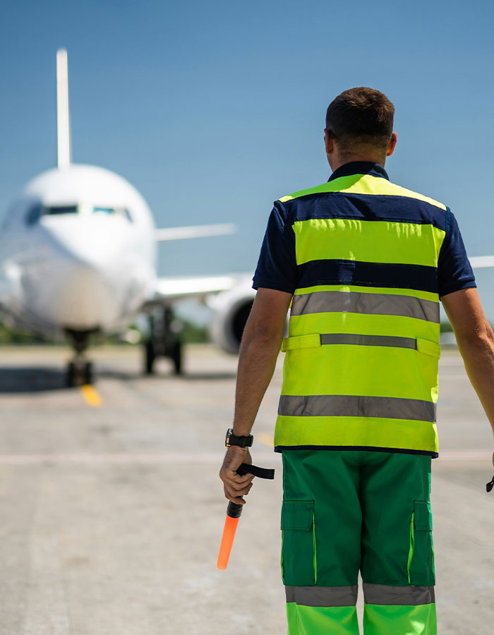 Airport ground crew member in high-visibility vest directing airplane before emergency landing caused by passenger scare on flight.
