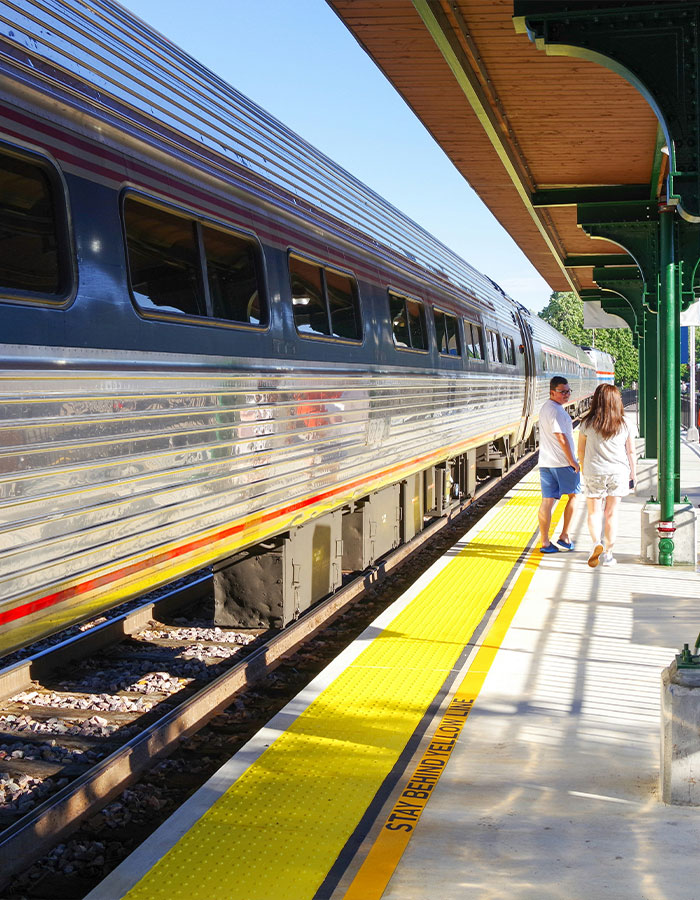 Train at a sunny station platform with two people walking near the yellow safety line, related to surf instructor accident incident.