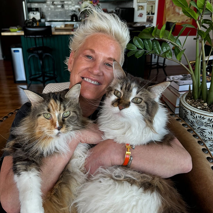 Master Chef Anne Burrell smiling and holding two fluffy cats in a cozy home setting. - 3